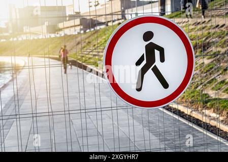 Kein Fußgängerschild hängt an Einem Metallzaundraht vor dem Hintergrund der Stadt Stockfoto