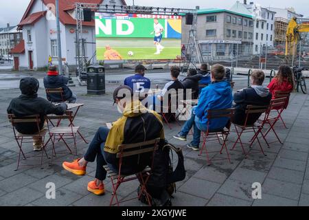 Nur wenige Fußballfans verfolgen bei regnerischem Wetter anlässlich der Fußball-Europameisterschaft UEFA EURO 2024 das Halbfinalspiel England gegen die Niederlande auf einer Leinwand auf dem Platz Hlemmur in Rsykajvik. / Nur wenige Fußballfans sehen das Halbfinalspiel zwischen England und den Niederlanden auf einem Bildschirm am Hlemmur-Platz in Rsykajvik bei regnerischem Wetter während der UEFA EURO 2024-Europameisterschaft. UEFA Fußball-Europameisterschaft - Fußballfans *** nur wenige Fußballfans sehen das Halbfinalspiel zwischen England und den Niederlanden auf einem Bildschirm bei Hlemmur S Stockfoto