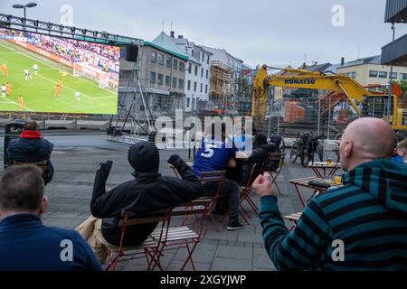 Nur wenige Fußballfans verfolgen bei regnerischem Wetter anlässlich der Fußball-Europameisterschaft UEFA EURO 2024 das Halbfinalspiel England gegen die Niederlande auf einer Leinwand auf dem Platz Hlemmur in Rsykajvik. / Nur wenige Fußballfans sehen das Halbfinalspiel zwischen England und den Niederlanden auf einem Bildschirm am Hlemmur-Platz in Rsykajvik bei regnerischem Wetter während der UEFA EURO 2024-Europameisterschaft. UEFA Fußball-Europameisterschaft - Fußballfans *** nur wenige Fußballfans sehen das Halbfinalspiel zwischen England und den Niederlanden auf einem Bildschirm bei Hlemmur S Stockfoto