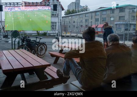 Nur wenige Fußballfans verfolgen bei regnerischem Wetter anlässlich der Fußball-Europameisterschaft UEFA EURO 2024 das Halbfinalspiel England gegen die Niederlande auf einer Leinwand auf dem Platz Hlemmur in Rsykajvik. / Nur wenige Fußballfans sehen das Halbfinalspiel zwischen England und den Niederlanden auf einem Bildschirm am Hlemmur-Platz in Rsykajvik bei regnerischem Wetter während der UEFA EURO 2024-Europameisterschaft. UEFA Fußball-Europameisterschaft - Fußballfans *** nur wenige Fußballfans sehen das Halbfinalspiel zwischen England und den Niederlanden auf einem Bildschirm bei Hlemmur S Stockfoto