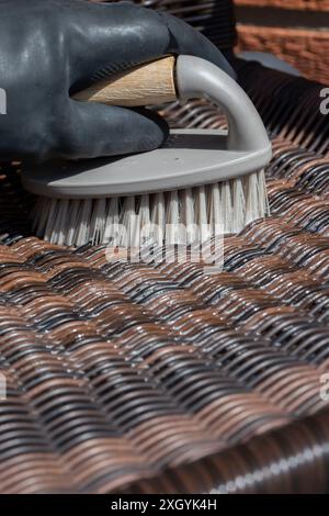 Person schrubbt Rattan-Patio-Stuhl mit einer Handbürste. Gartenheim Hausarbeit Chore Konzept. Stockfoto