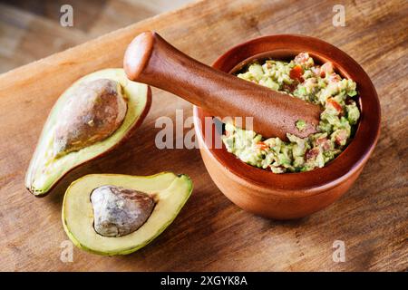 Nahaufnahme von Avocados und frischer hausgemachter Guacamole im Holzmörtel mit Stößel (Molcajete). Traditionelle mexikanische Sauce aus Reifen Avocados. Stockfoto
