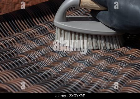 Person schrubbt Rattan-Patio-Stuhl mit einer Handbürste. Gartenheim Hausarbeit Chore Konzept. Stockfoto