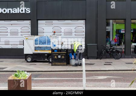 Belfast, County Antrim Nordirland 05. Juli 2024 - Gemeindeangestellter leert Abfalleimer auf einer Straße im Stadtzentrum vor einem großen Einzelhandelsgeschäft Stockfoto