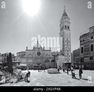 Helles Sonnenlicht, das hinter der Fassade der Kirche und ihrem Glockenturm in den campo Santa Maria Formosa hinunterstrahlt, die Menschen genießen den Platz Stockfoto