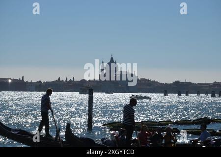 Zwei Gondoliere rudern ihre Gondeln mit Sonnenlicht auf dem Wasser und Chiesa del Santissimo Redentore auf Giudecca über dem Becken von St. Markus, Venedig Stockfoto