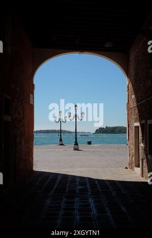 Ein Blick durch eine bogenförmige Fahrbahn nach Riva dei Sette Martiri, zwei Straßenlaternen und das blaue Wasser der Lagune von Venedig an einem hellen Sommertag Stockfoto