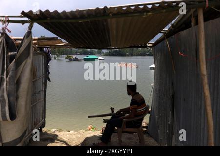 11. Juli 2024, Kurigram, Kurigram, Bangladesch: Ein Mann sitzt in einer provisorischen Hütte auf der Straße und blickt auf sein überflutetes Haus im Dorf Jatrapur, Kurigram. Der Fluss Dharla im Stadtteil Kurigram von Bangladesch hat alle Häuser in den tiefgelegenen Gebieten überflutet, da das Wasser die Gefahrengrenze überschritten hat. Fast zwei Seenopfer aus 400 Dörfern von 55 Gewerkschaften von 9 Utopazilas des Bezirks Kurigram leben aufgrund von Überschwemmungen zwei Wochen lang ein armseliges Leben. Im Norden Bangladeschs kam es zu Überschwemmungen, da die Wasserstände in Flüssen aufgrund von starken Regenfällen flussaufwärts steigen. Die Menschen, die in diesen Häusern leben, haben in der Th Zuflucht gefunden Stockfoto