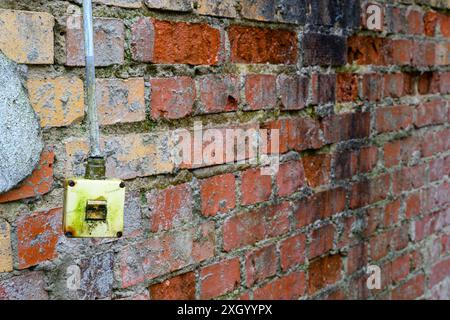 Der alte elektrische Schalter hängt lose vor einer Ziegelwand Stockfoto