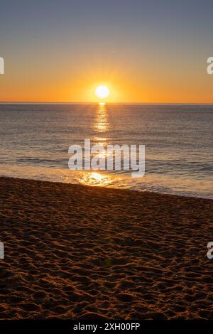 Die ersten Sonnenstrahlen berühren sanft den Horizont und beleuchten das ruhige Wasser von Canet Beach. Die ruhige morgendliche Atmosphäre ist festgehalten Stockfoto