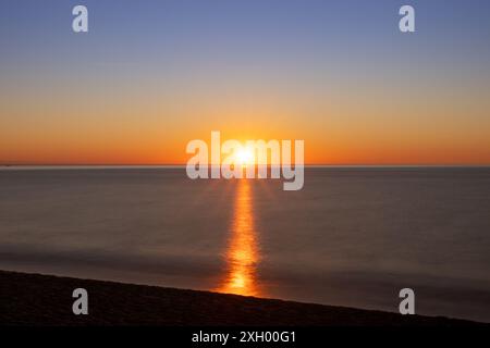 Die goldenen Strahlen der aufgehenden Sonne erleuchten Canet Beach und werfen ein warmes Licht auf das ruhige Meer. Die friedliche Atmosphäre am frühen Morgen Stockfoto