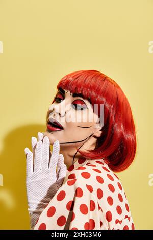 Eine hübsche rothaarige Frau mit Pop-Art-Make-up und einem Tupfen-Kleid auf gelbem Hintergrund, das einer Figur aus Comics ähnelt. Stockfoto