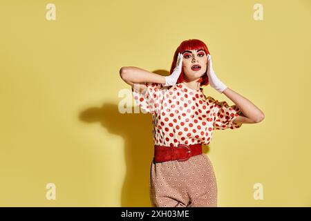 Eine hübsche rothaarige Frau mit kreativem Pop Art Make-up in einem Polka Dot Shirt auf gelbem Hintergrund. Stockfoto