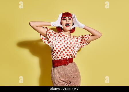 Eine hübsche rothaarige Frau mit Pop-Art-Make-up in einem Polka-Dot-Shirt auf gelbem Hintergrund, ähnlich einer Figur aus Comics. Stockfoto