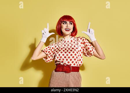 Eine hübsche rothaarige Frau mit Pop-Art-Make-up in einer Bluse mit Punktmuster und weißen Handschuhen auf gelbem Hintergrund. Stockfoto