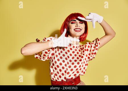 Eine stilvolle rothaarige Frau mit Pop-Art-Make-up, die ein Polka Dot-Shirt und weiße Handschuhe vor gelbem Hintergrund trägt. Stockfoto