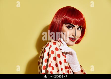 Eine rothaarige Frau in einem gepunkteten Kleid posiert vor einem leuchtend gelben Hintergrund und strahlt eine skurrile Comic-Atmosphäre aus. Stockfoto