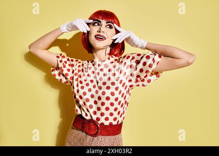 Eine hübsche rothaarige Frau in einem Polka Dot Top hebt sich vor einem gelben Hintergrund hervor und ihr Pop Art Make-up verleiht eine Comic-Charakter-Atmosphäre. Stockfoto