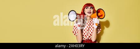 Rothaarige Frau im Clown Kostüm mit Megaphon, kreatives Pop Art Make-up, Polka Dot Bluse, auf gelbem Hintergrund. Stockfoto