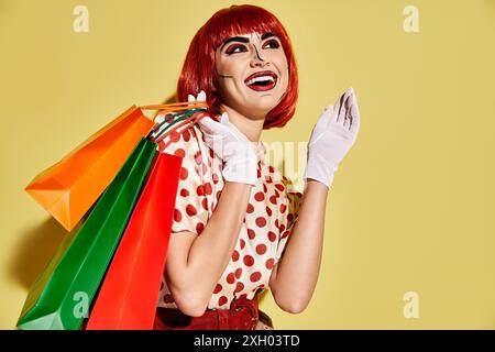 Eine hübsche rothaarige Frau mit kreativem Pop-Art-Make-up, die Einkaufstaschen auf gelbem Hintergrund hält. Stockfoto