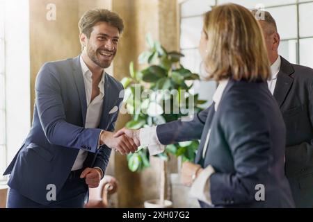 Lächelnder Geschäftsmann, der Kollegen in modernen Büros die Hand schüttelt. Professionelle Begrüßung, erfolgreiche Partnerschaft. Unternehmensumfeld mit natürlicher Natur Stockfoto