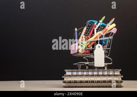 Back-to-School-Vorlage mit mehrfacher Schreibwaren im Wagen mit Kopierraum vor schwarzem Hintergrund. Hintergrund des Bildungskonzepts mit Kopierraum. Stockfoto