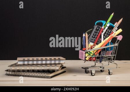 Back-to-School-Vorlage mit mehrfacher Schreibwaren im Wagen mit Kopierraum vor schwarzem Hintergrund. Hintergrund des Bildungskonzepts mit Kopierraum. Stockfoto