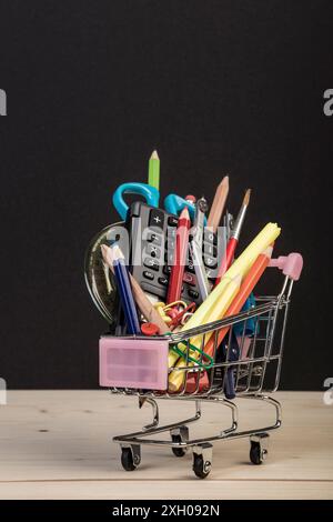 Back-to-School-Vorlage mit mehrfacher Schreibwaren im Wagen mit Kopierraum vor schwarzem Hintergrund. Hintergrund des Bildungskonzepts mit Kopierraum. Stockfoto