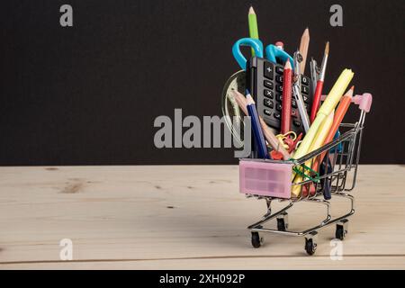 Back-to-School-Vorlage mit mehrfacher Schreibwaren im Wagen mit Kopierraum vor schwarzem Hintergrund. Hintergrund des Bildungskonzepts mit Kopierraum. Stockfoto