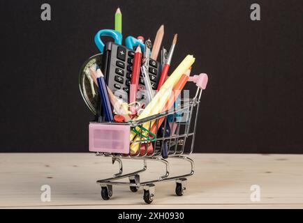 Back-to-School-Vorlage mit mehrfacher Schreibwaren im Wagen mit Kopierraum vor schwarzem Hintergrund. Hintergrund des Bildungskonzepts mit Kopierraum. Stockfoto