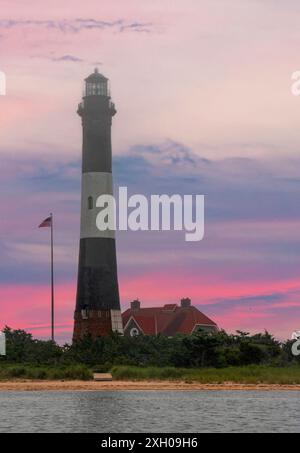 Ein hoher, schwarz-weißer Leuchtturm steht markant am Wasser, mit einer amerikanischen Flagge in der Nähe und einem Gebäude, das sich zwischen Bäumen im Hintergrund verbirgt. Stockfoto