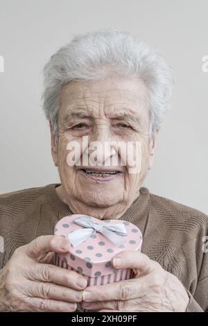 Eine reizende Seniorin, die eine herzförmige Geschenkbox hält Stockfoto