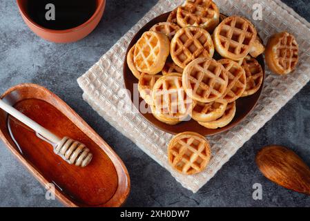 Runde Waffeln auf einem Teller, Kaffee und Honig auf einem grauen Tisch Stockfoto