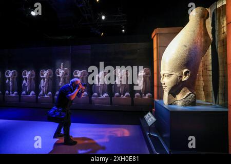 Köln, Deutschland. Juli 2024. Ein Mann fotografiert eine Kollosalstatue von Ramses II. Im Odysseum. Die Ausstellung „Ramses & das Gold der Pharaonen“ ist ab 13. Juni 2024 in Köln zu sehen. Das Herzstück ist der echte Sarkophag von Ramses II. Alle Objekte stammen aus Museen und historischen Stätten in Ägypten. Quelle: Oliver Berg/dpa/Alamy Live News Stockfoto