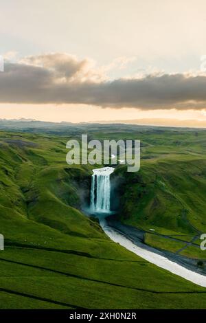 Luftaufnahme des Skogafoss Wasserfalls in Island bei Sonnenuntergang, umgeben von üppigen grünen Landschaften und dramatischem Himmel. Stockfoto