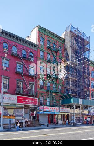 NYC Chinatown: Ein begehbares Wohnhaus aus Ziegelstein mit chinesischen Schildern auf den Straßenläden; die Terrakotta und die Feuertreppe sind grün gestrichen. Stockfoto