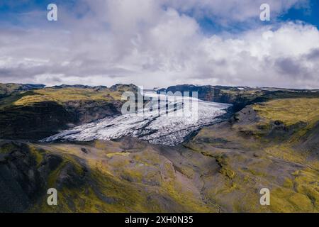 Blick aus der Vogelperspektive auf den Solheimajokull-Gletscher in Island, mit leuchtend grünen, moosbedeckten Bergen, die im Kontrast zum scharf weißen Gletscher stehen Stockfoto