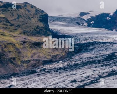 Blick aus der Vogelperspektive auf den Solheimajokull-Gletscher in Island, mit leuchtend grünen, moosbedeckten Bergen, die im Kontrast zum scharf weißen Gletscher stehen Stockfoto