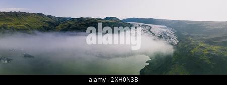 Ein Panoramablick auf den Sólheimajokull-Gletscher in Island, mit üppigen grünen Bergen, einer Gletscherlagune und einer Nebelschicht. Stockfoto