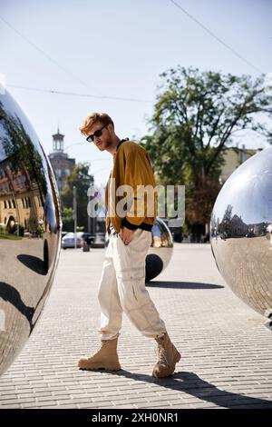 Ein junger rothaariger Mann in dämlicher Kleidung, der an zwei glänzenden Kugeln vorbeischlendert. Stockfoto