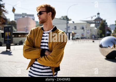 Junger Mann mit roten Haaren und unbändiger Kleidung, überkreuzte Arme, mitten auf der Straße stehend. Stockfoto