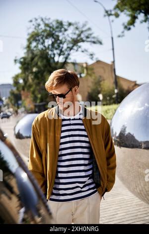 Ein junger rothaariger Mann in brauner Kleidung steht mit Sonnenbrille auf einem Bürgersteig. Stockfoto