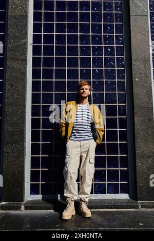 Ein stilvoller rothaariger Mann steht selbstbewusst vor einem hoch aufragenden Stadtgebäude. Stockfoto