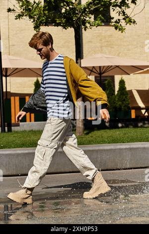 Ein stilvoller junger Mann mit rotem Haar überquert eine Stadtstraße neben einem Brunnen. Stockfoto