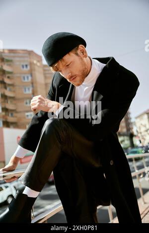 Ein rothaariger Mann in unbändiger Kleidung und ein Hut, der anmutig auf einem Felsvorsprung in der Stadt sitzt. Stockfoto