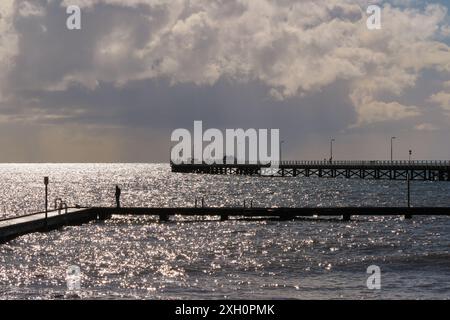 Atmosphärisches Licht und Wolken mit Regenschauern mit dem Hauptanleger Busselton und einem Mann auf dem kleineren Steg, Busselton, Western Australia. Stockfoto