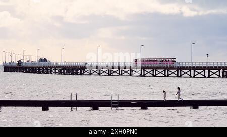 Der Bootszug auf dem Busselton Jetty und zwei Kinder auf dem kleineren Bootssteg bei atmosphärischen Bedingungen am Busselton Foreshore, Western Australia. Stockfoto