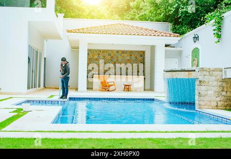 Mann, der das Schwimmbad mit Saugschlauch reinigt. Poolpflege und -Reinigung mit Staubsaugerschlauch. Reinigung und Wartung des Schwimmbades Stockfoto