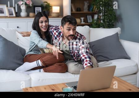 Junges glückliches Paar, einfaches Leben, zu Hause auf dem Sofa sitzen, Filme auf dem Laptop auswählen und anschauen, Popcorn essen und gemeinsame Zeit genießen. Er Stockfoto