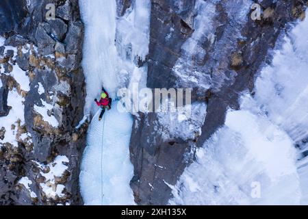 Die Frau legt eine Eisschraube auf. Eisklettern auf dem gefrorenen Wasserfall, Aerial View Stockfoto